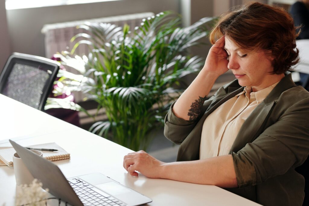 woman rubbing her temples at a computer desk, frustrated and tired
