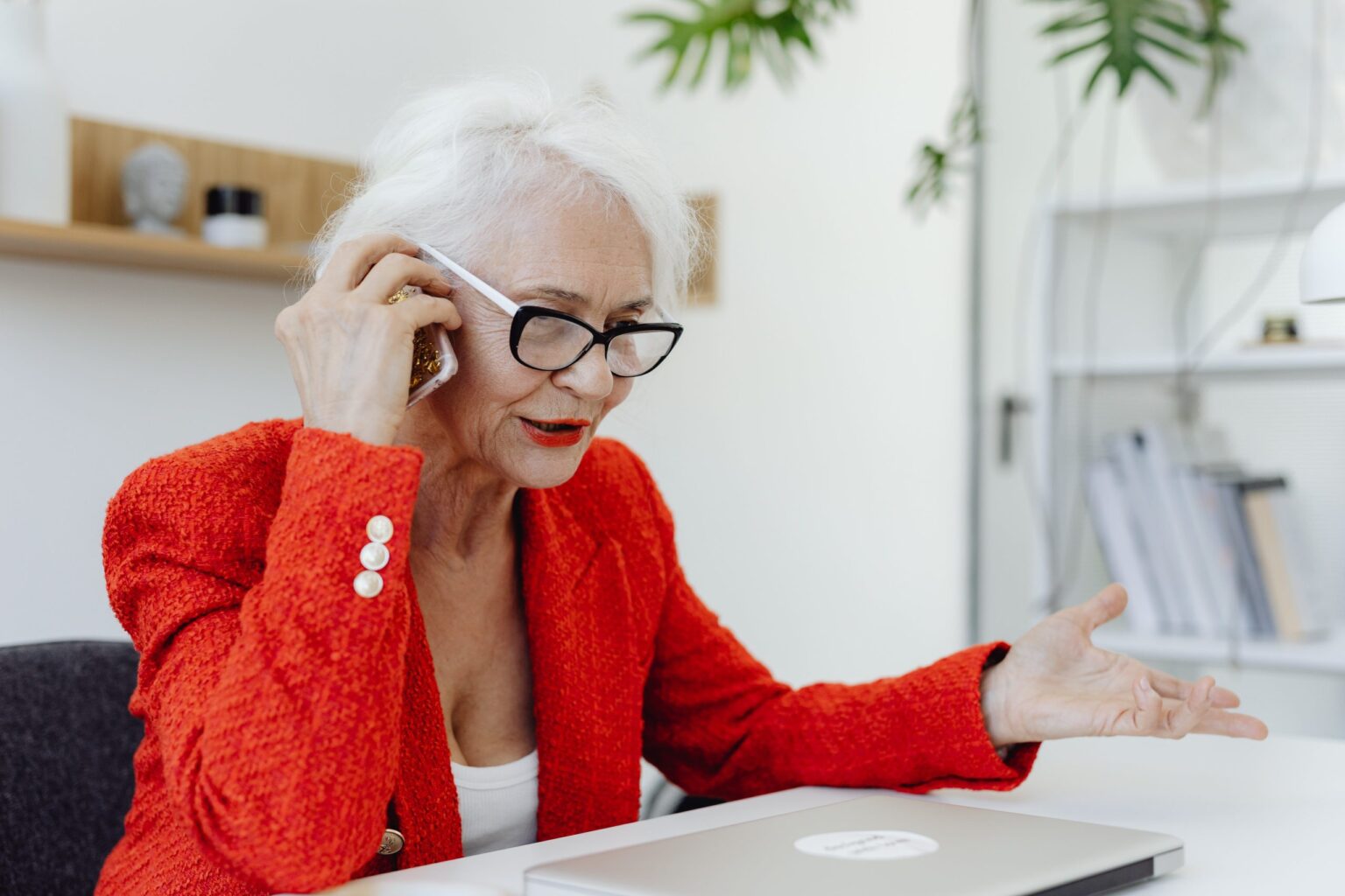 a business woman in a red blazer jacket makes an important call on her iphone at her work desk