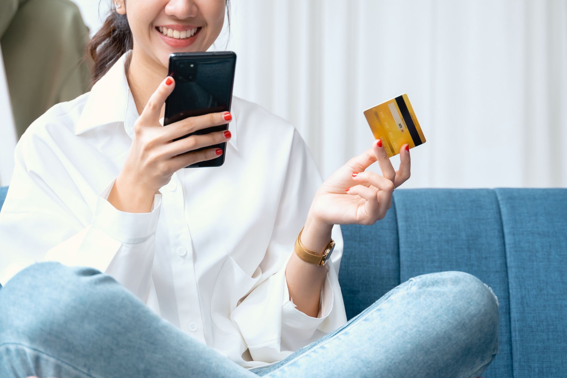 a smiling woman holds a credit card in one hand, a mobile phone in the other