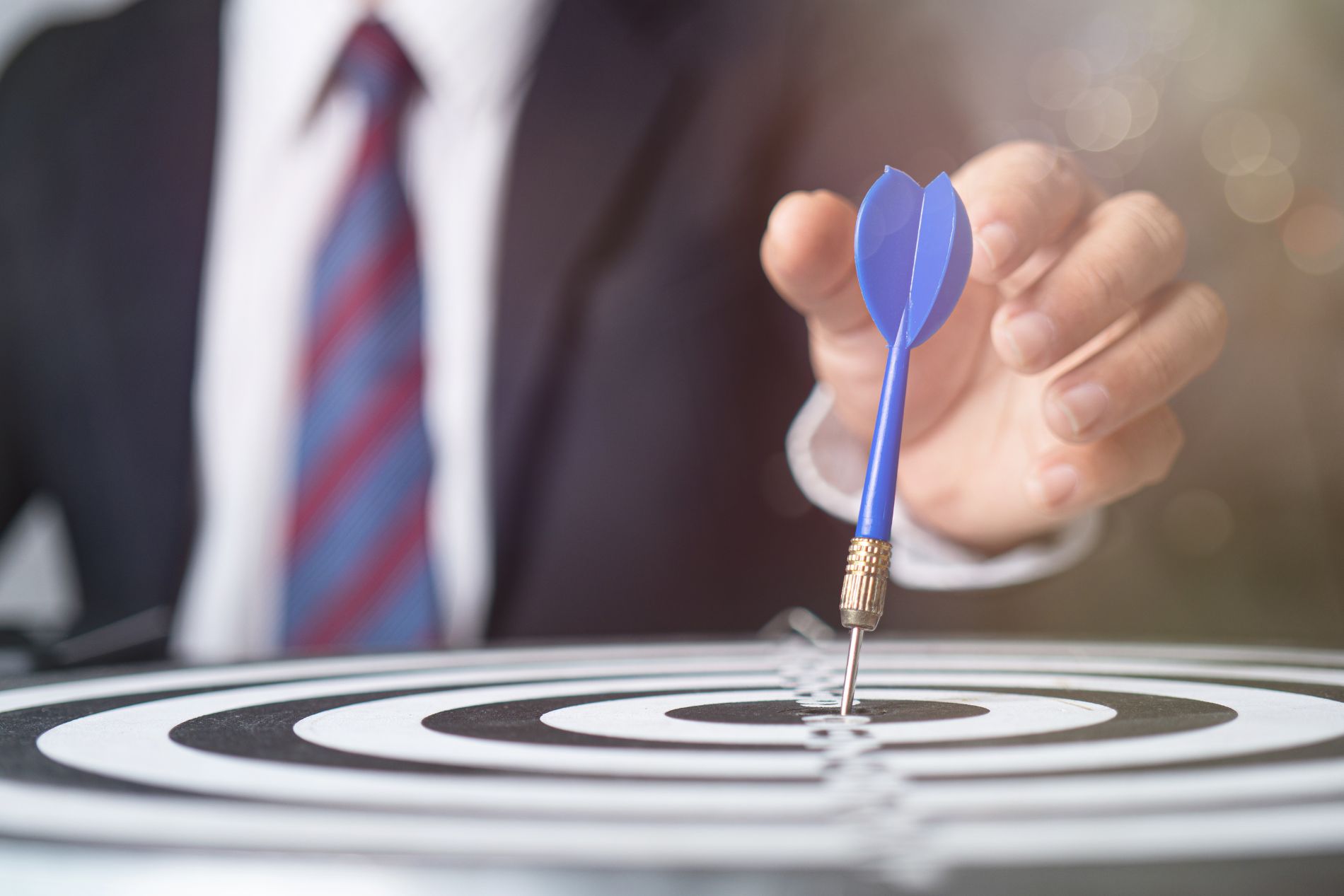 a person in a business suit, behind a dartboard with a dart in the centre
