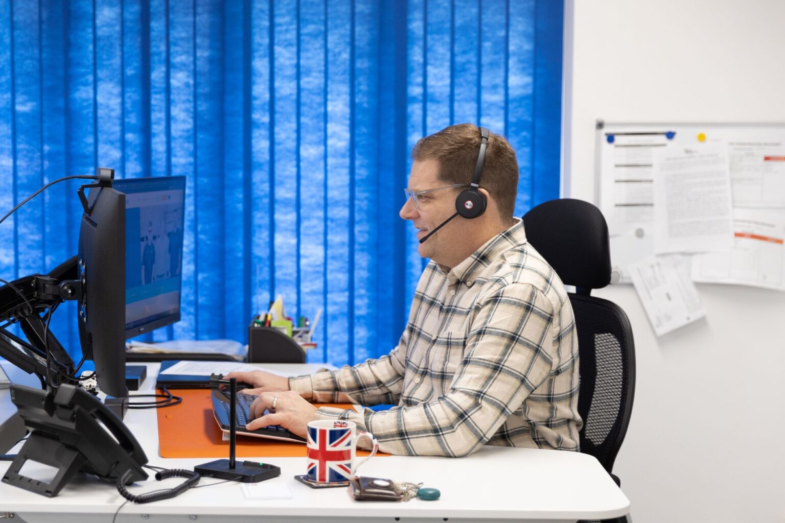 Jon is pictured smiling in business casual wear, at his office desk with a headset on
